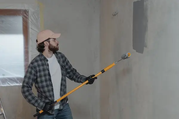 Painter rolling grey paint onto an interior wall in Anchorage